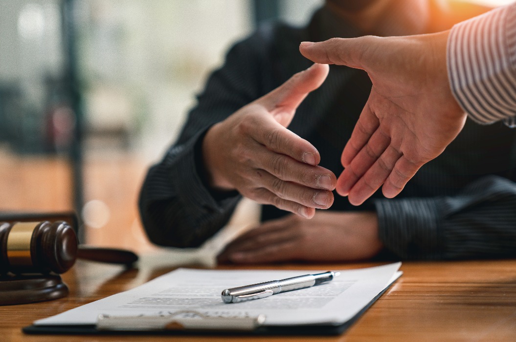 Rechtsanwälte geben Geschäftsleuten die Hand, um eine Vereinbarung zu besiegeln.